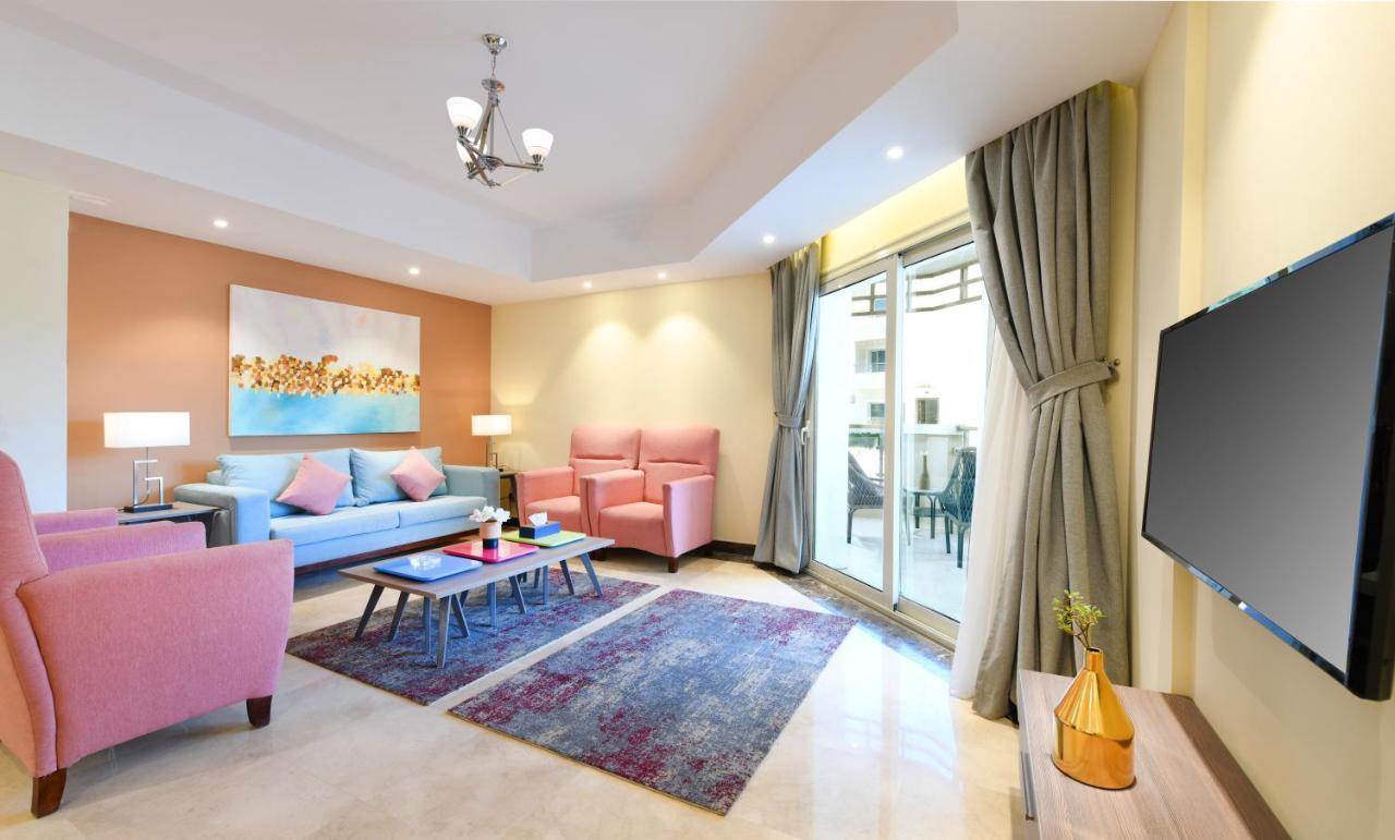منتجع توليب الجلالة ماجستيك عين السخنة الغرفة الصورة The photo shows a modern living room that features a cozy and stylish design. There is a light blue sofa adorned with pastel pink cushions, accompanied by two pink armchairs. A coffee table sits in front, placed on a colorful area rug that adds warmt