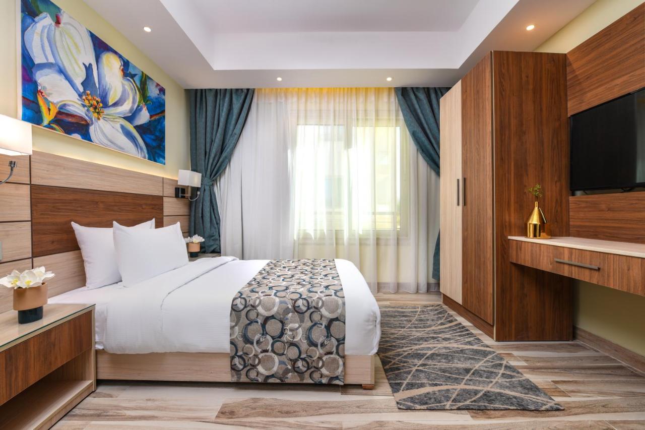منتجع توليب الجلالة ماجستيك عين السخنة المظهر الخارجي الصورة The photo shows a well-designed hotel room. It features a comfortable bed with a decorative bedspread and two pillows. There are soft curtains framing a window that lets in natural light. On one side, there is a colorful piece of artwork hanging on t