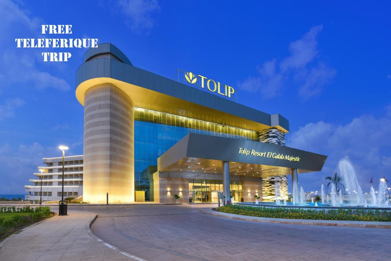 منتجع توليب الجلالة ماجستيك عين السخنة المظهر الخارجي الصورة The photo shows a modern hotel building named "Tolip Resort & Spa," featuring a sleek architectural design with large glass windows. The hotel is illuminated against a twilight sky, showcasing its prominent signage. In the foreground, there is a well