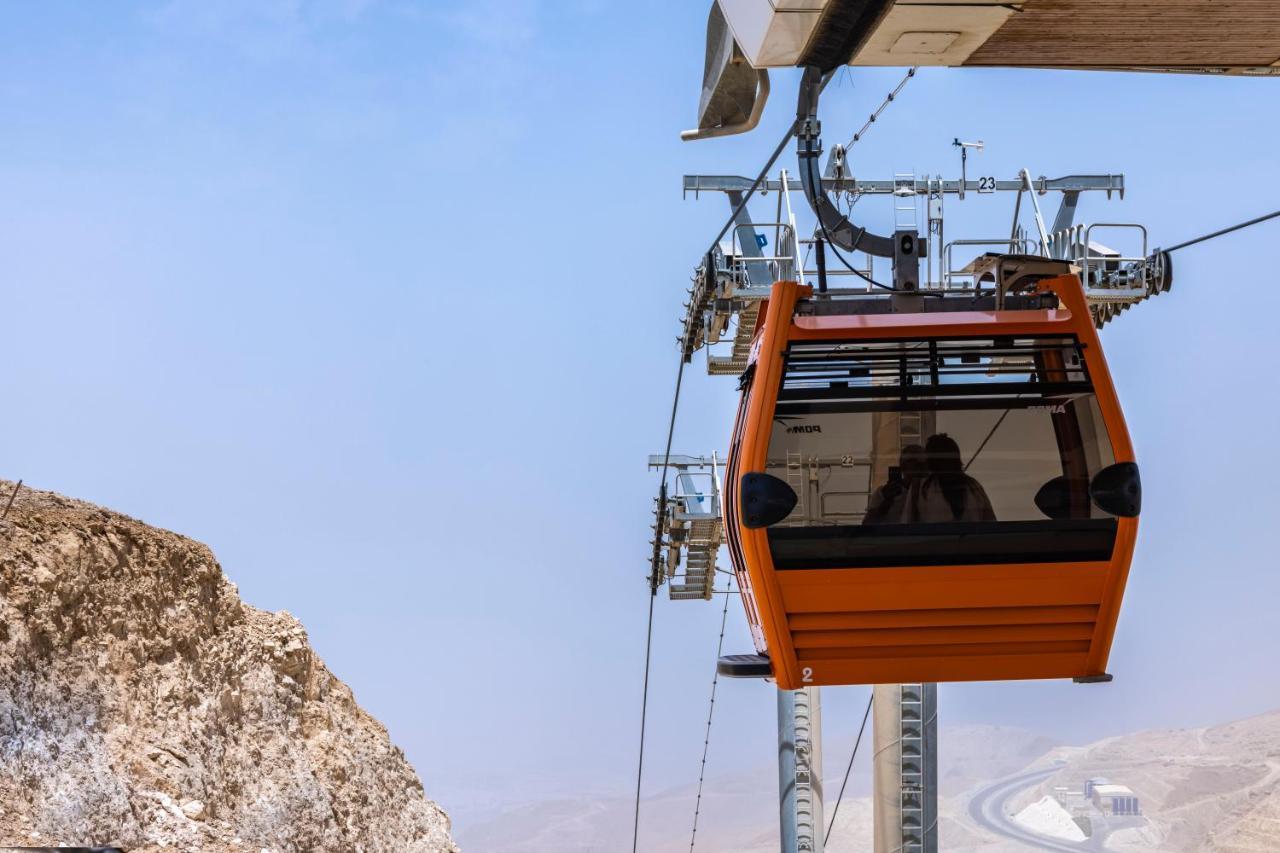 منتجع توليب الجلالة ماجستيك عين السخنة المظهر الخارجي الصورة The photo shows an orange gondola or cable car hanging on a cable system. The gondola appears to be suspended in the air above a rocky landscape, with a clear sky in the background. There are supporting cables and structures visible, indicating that 
