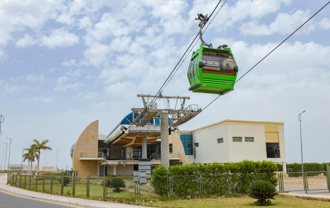 منتجع توليب الجلالة ماجستيك عين السخنة المظهر الخارجي الصورة The photo shows a cable car or gondola system in operation, featuring a green-colored gondola. It is suspended from cables and moving towards a station, which appears to be a modern building with a unique architectural design. The station has large w