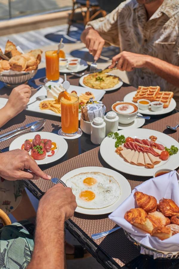 منتجع توليب الجلالة ماجستيك عين السخنة المظهر الخارجي الصورة The photo features a spread of breakfast dishes on a table. There are two sunny-side-up eggs on one plate, surrounded by various food items, including slices of ham, sausages, and fresh tomatoes. Another plate holds a serving of waffles. A bowl with 
