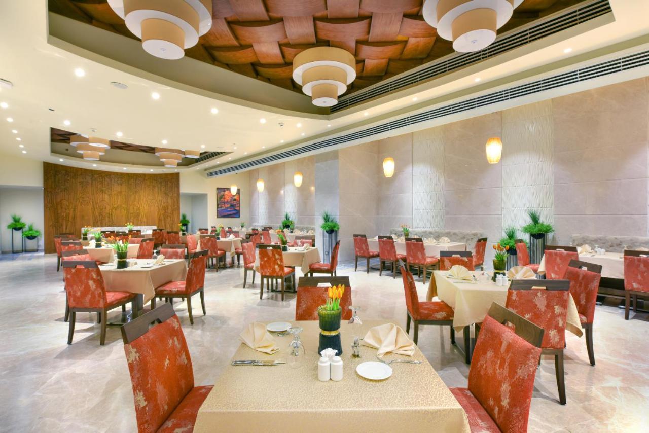 منتجع توليب الجلالة ماجستيك عين السخنة المظهر الخارجي الصورة The photo shows the interior of a restaurant. The space features several tables set with light-colored tablecloths and chairs with reddish upholstery. Each table is adorned with decorative napkins and has small plants in the center. The room has a mo