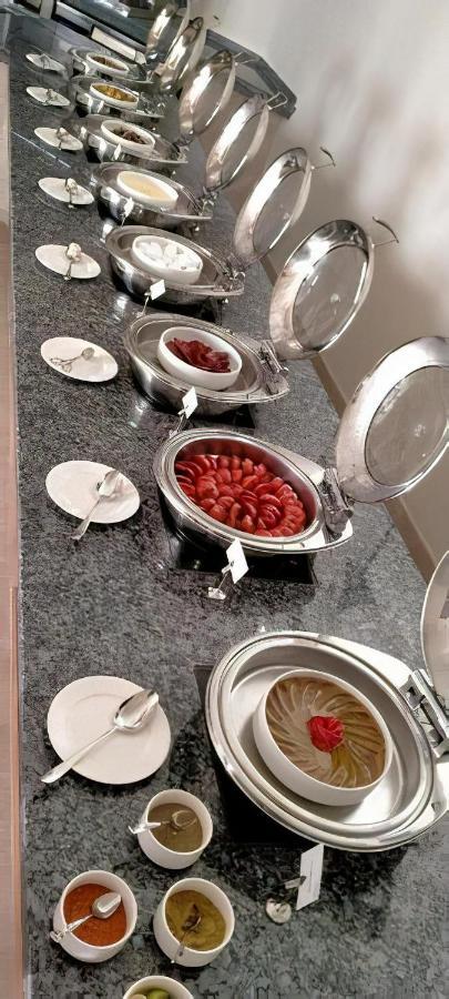 منتجع توليب الجلالة ماجستيك عين السخنة المظهر الخارجي الصورة The photo shows a buffet setup featuring multiple metal serving trays on a dark granite countertop. One tray contains circular slices of food, possibly sausages or a similar dish, while another bowl holds what appears to be red food items, though it'