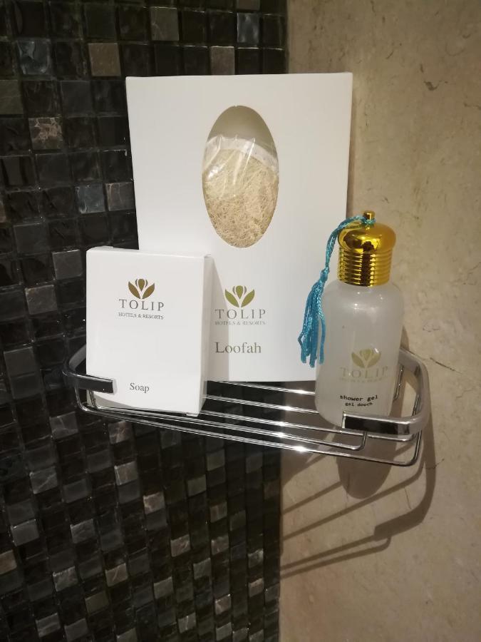 منتجع توليب الجلالة ماجستيك عين السخنة المظهر الخارجي الصورة The photo shows a small metal shelf containing three items related to personal care. 

1. **Soap**: A white box labeled "TOLIP" with the word "Soap" visible on the front.
2. **Loofah**: A package with the same "TOLIP" branding, containing loofah.
3. 