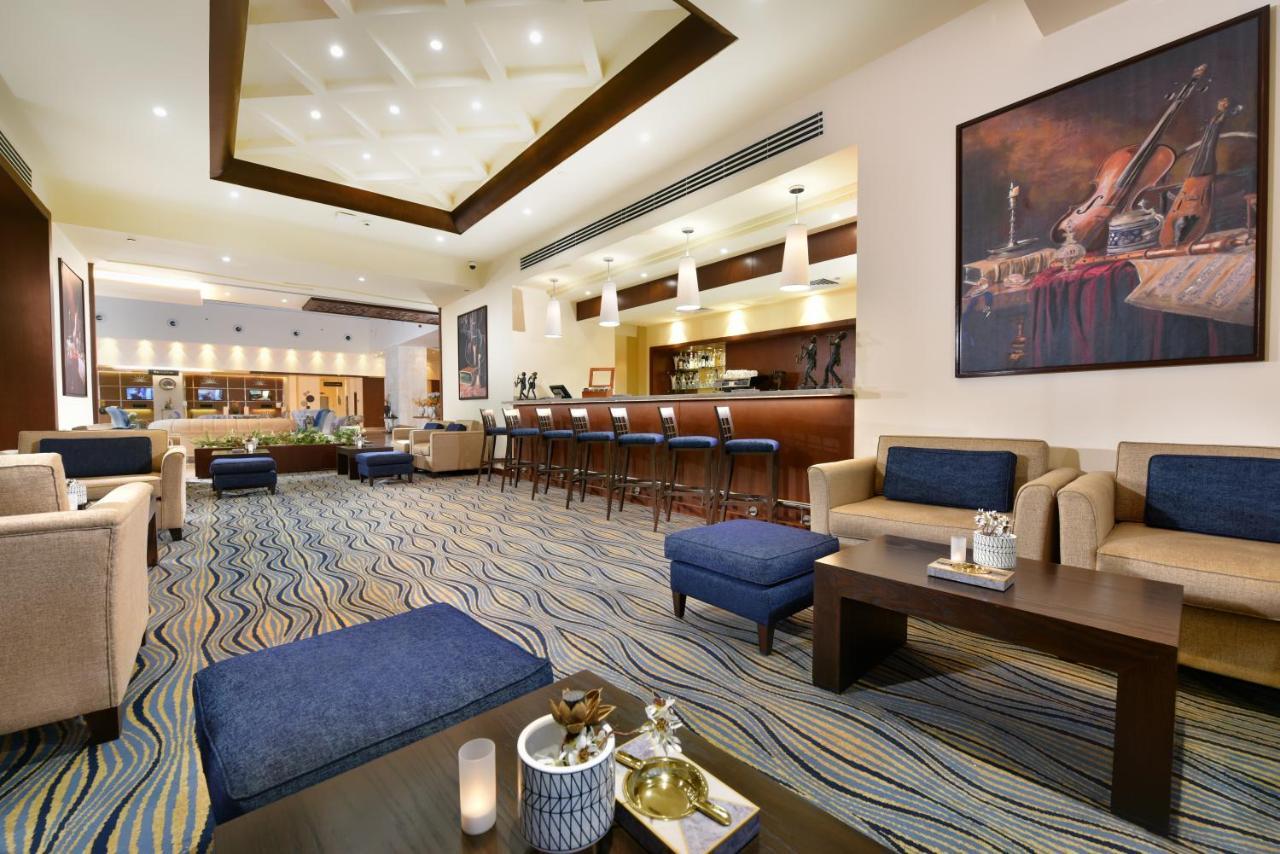 منتجع توليب الجلالة ماجستيك عين السخنة المظهر الخارجي الصورة The photo depicts a modern, inviting lobby or lounge area. It features a cozy seating arrangement with light-colored sofas and deep blue accent chairs. In the center, there is a low wooden coffee table with decorative items, including a candle and sm
