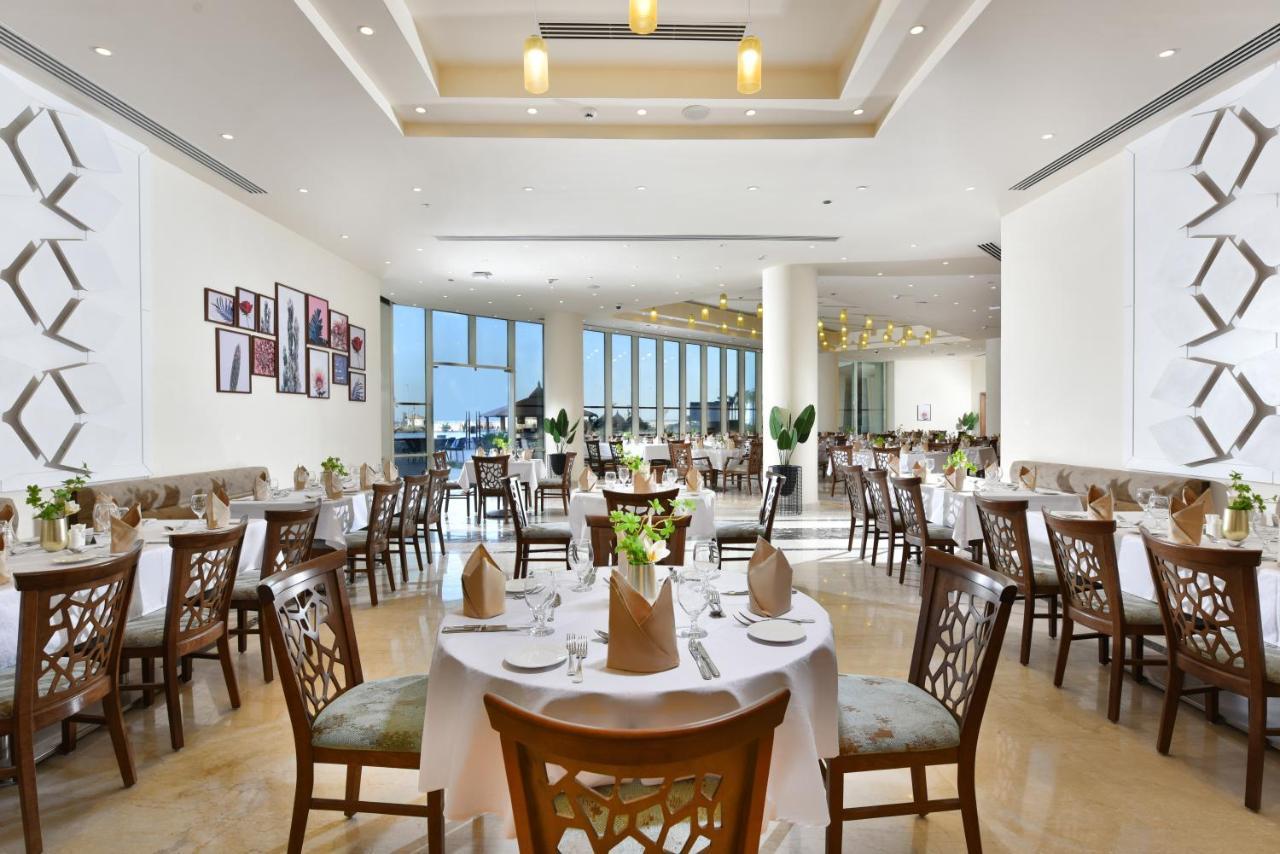 منتجع توليب الجلالة ماجستيك عين السخنة المظهر الخارجي الصورة The photo displays a spacious and elegantly designed restaurant interior. It features numerous tables set for dining, with white tablecloths, neatly folded napkins, and decorative centerpieces of flowers. The seating consists of wooden chairs that co